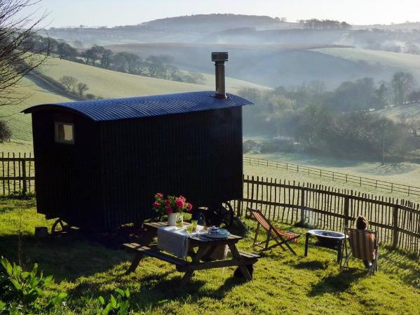 Outdoor view of hut with picnic bench & seating overlooking countryside